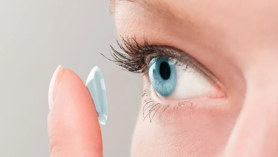 Contact lens on a fingertip in front of a blue eye