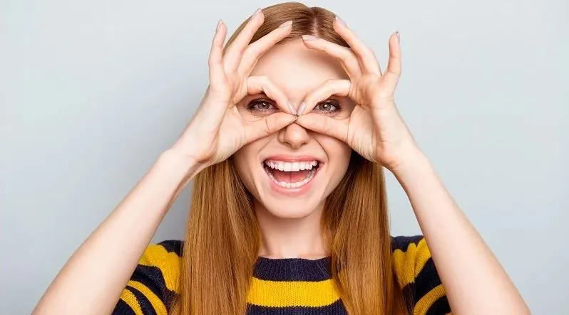 Smiling woman forming glasses with her hands after laser eye surgery